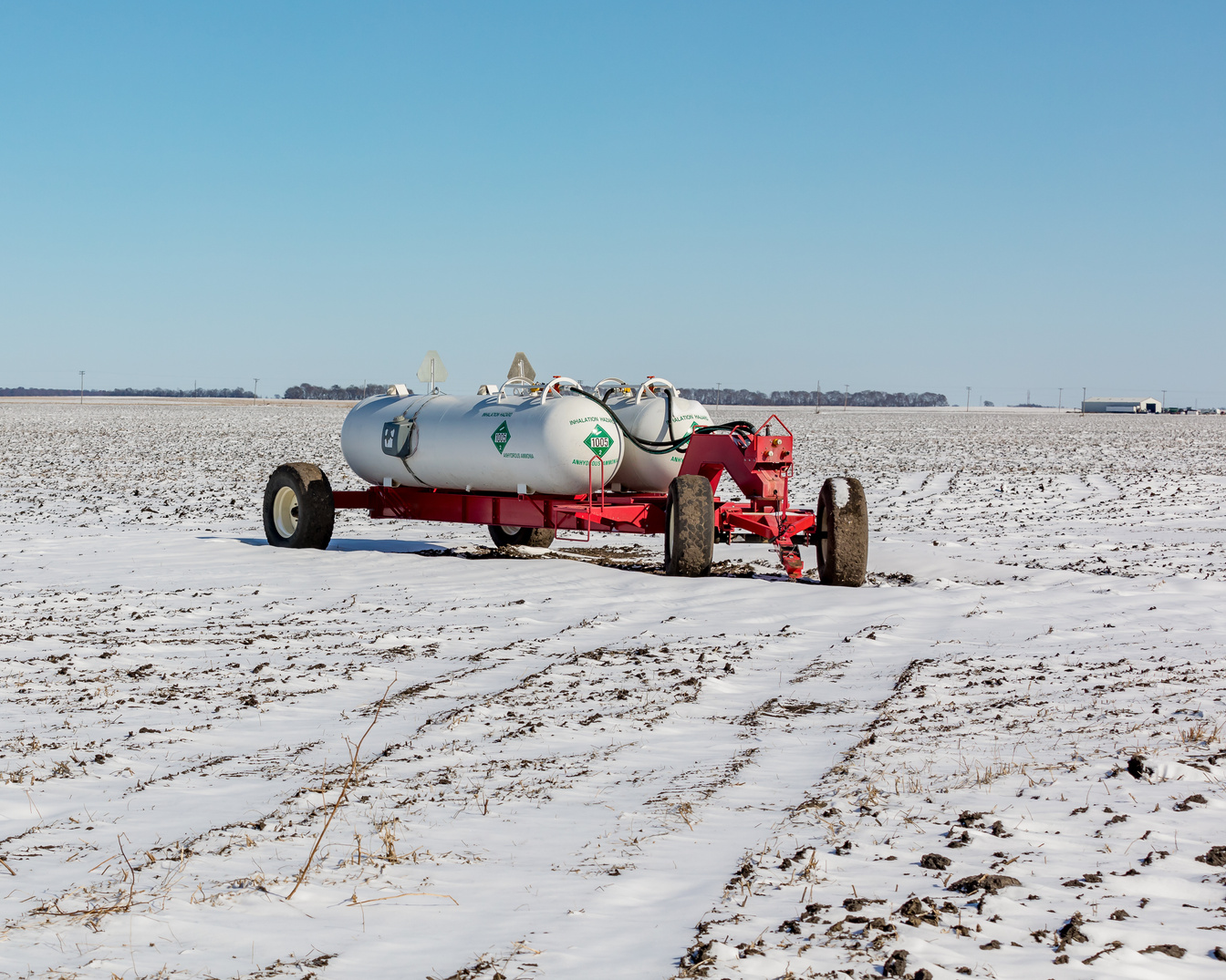 Anhydrous ammonia fertilizer tanks and wagon in harvested soybean farm field covered in snow after an eary winter snowstorm